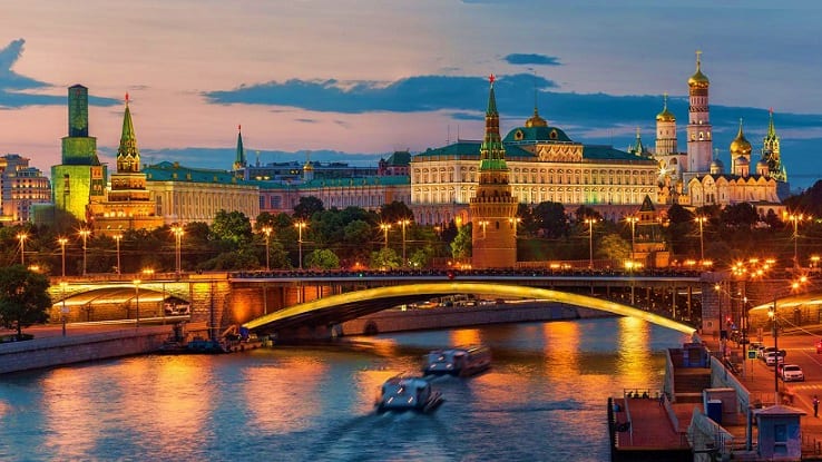 Moscow Kremlin and illuminated bridge over Moscow River at dusk with golden-lit historic buildings and churches